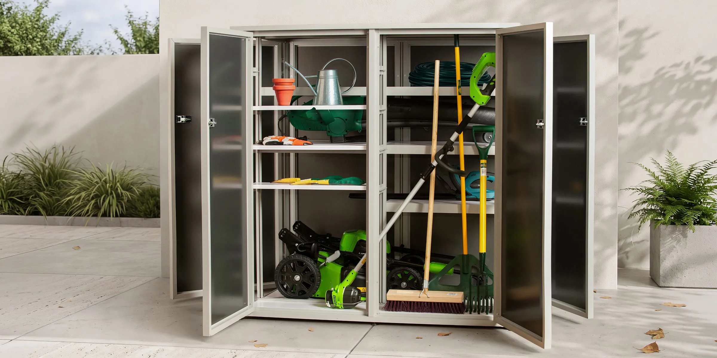 Type M outdoor storage unit in White on a patio, all doors open with a lawnmower, garden tools and a watering can inside