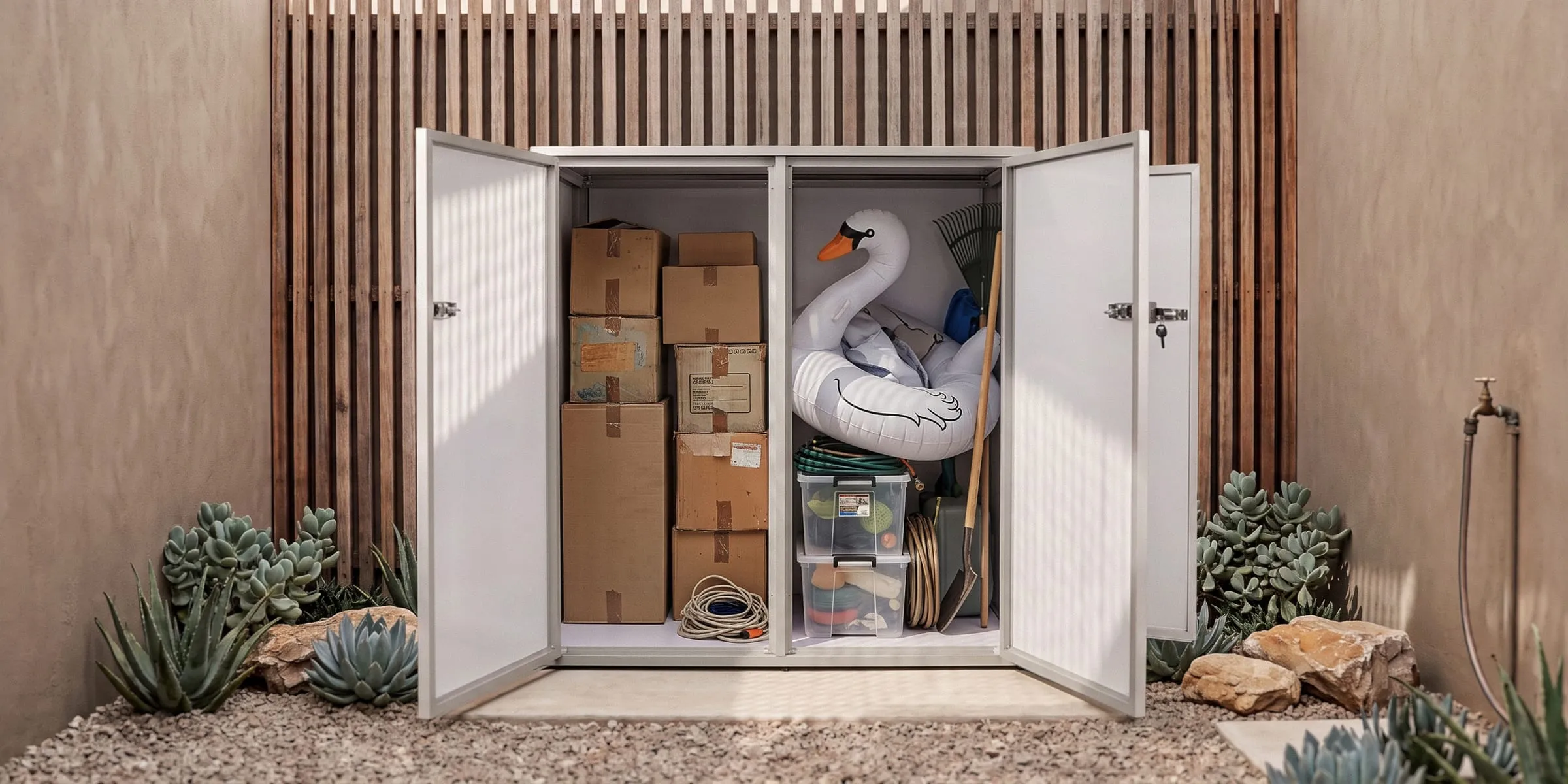 Type U outdoor storage unit in White in a courtyard, doors open with boxes, a pool float and garden tools inside